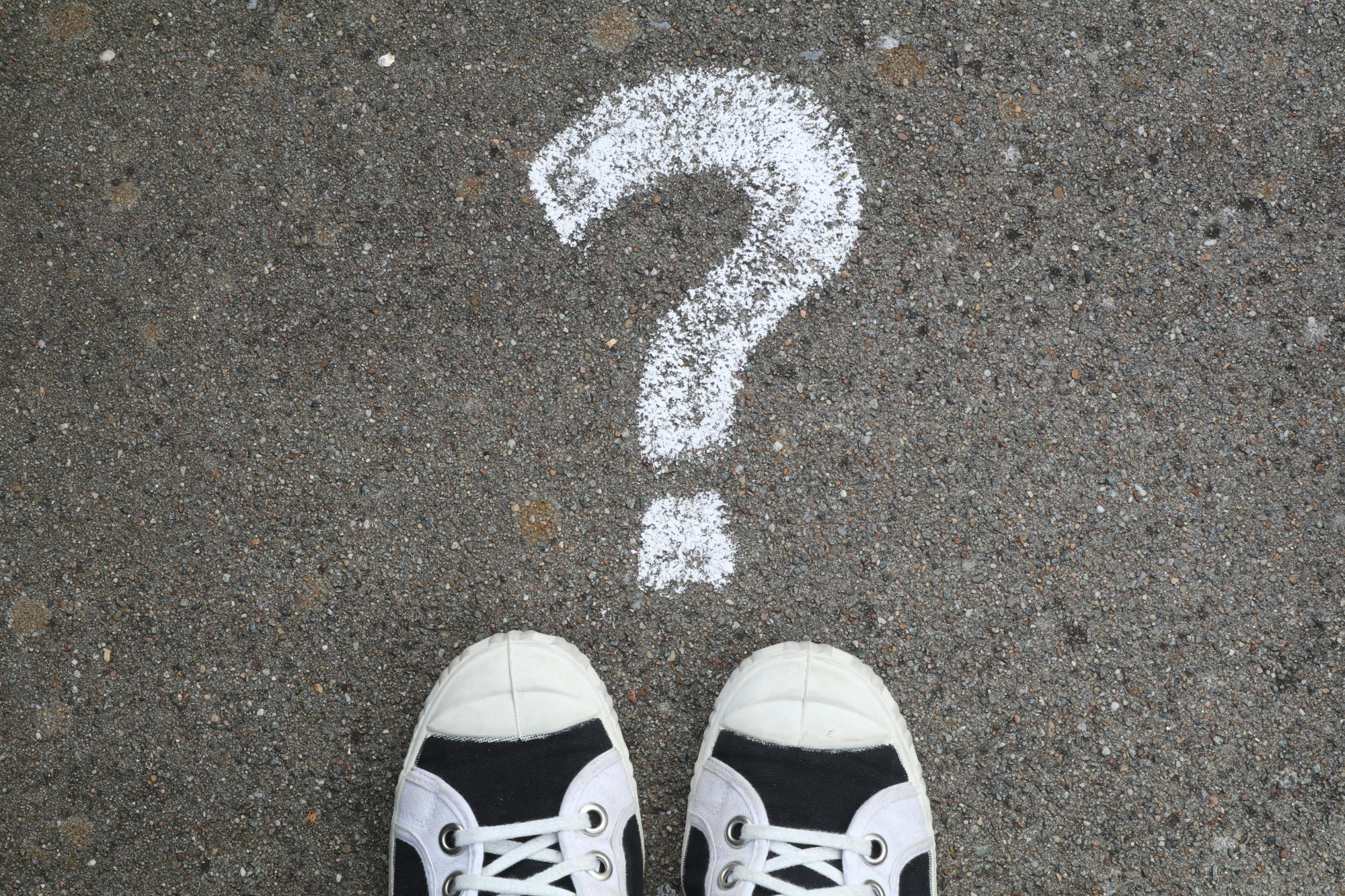 Chalk question mark on the ground with two feet stood in front of it.